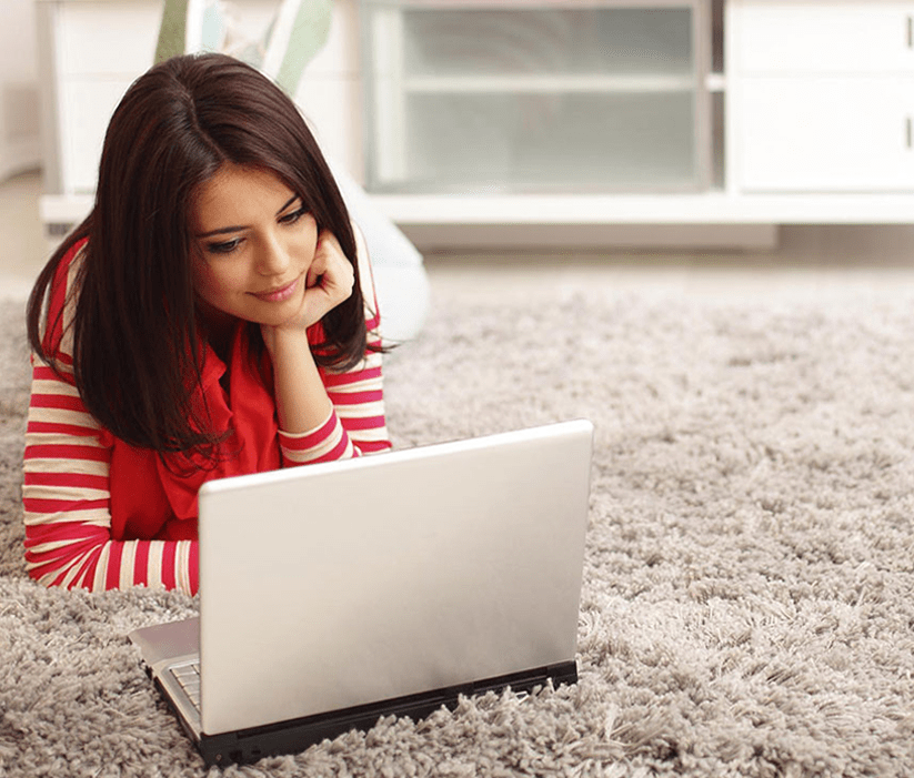 Young woman lying on a soft carpet, using a laptop